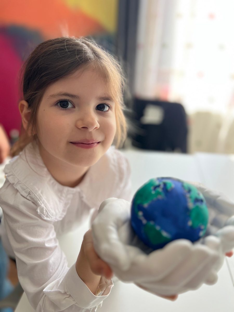 Fetiță care ține în palme o planetă Pământ modelată din plastilină