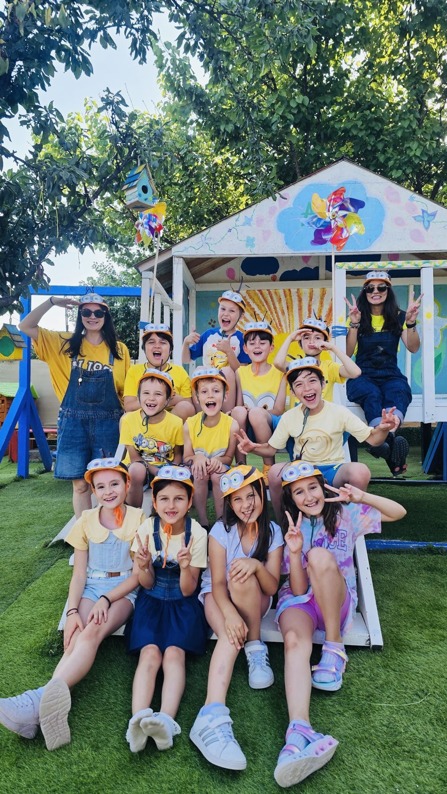Copiii și educatoarele la un sleepover ABC, cu pălării galbene, în curte