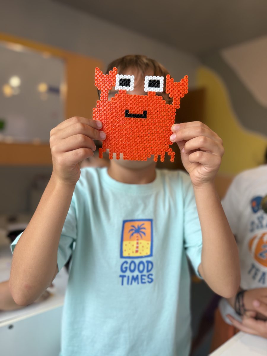 Copil care arată un crab făcut din mărgele